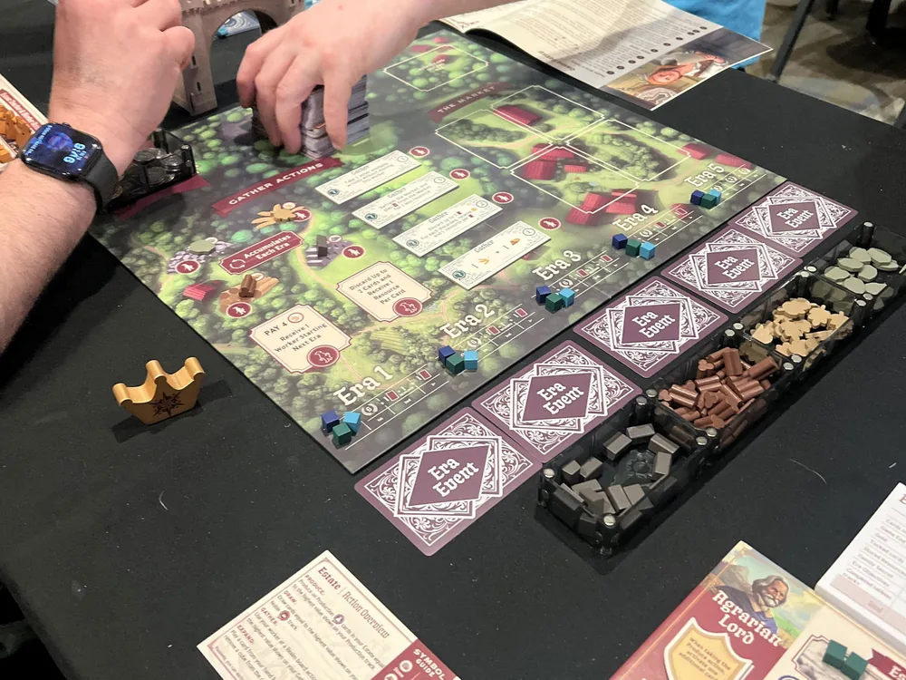 A game in progress at Origins Game Fair with resources sorted into Piece Keepers trays beside the board
